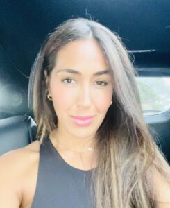 Woman with long hair in a black sleeveless top, smiling inside a vehicle.