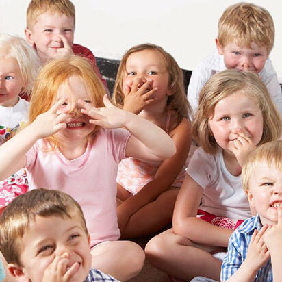 A group of children sitting on the floor and covering their mouths.